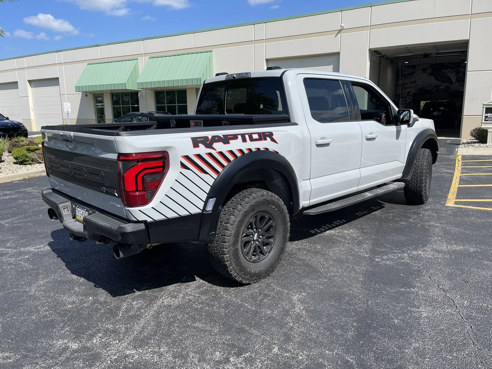 White pickup truck with Raptor branding parked outside a commercial building with green awnings.