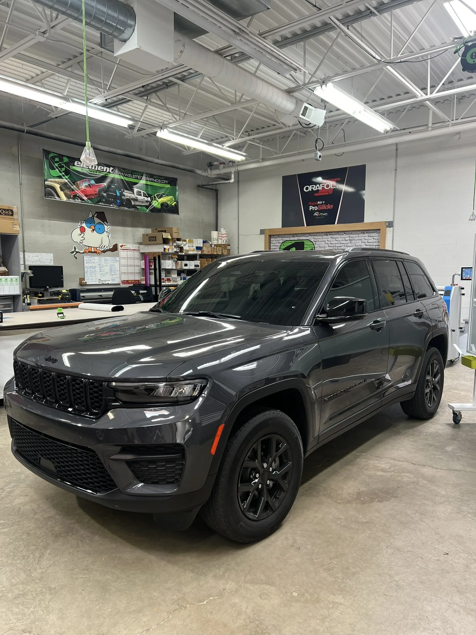 Gray Jeep SUV parked inside an automotive service center or garage with various signs and equipment in the background.