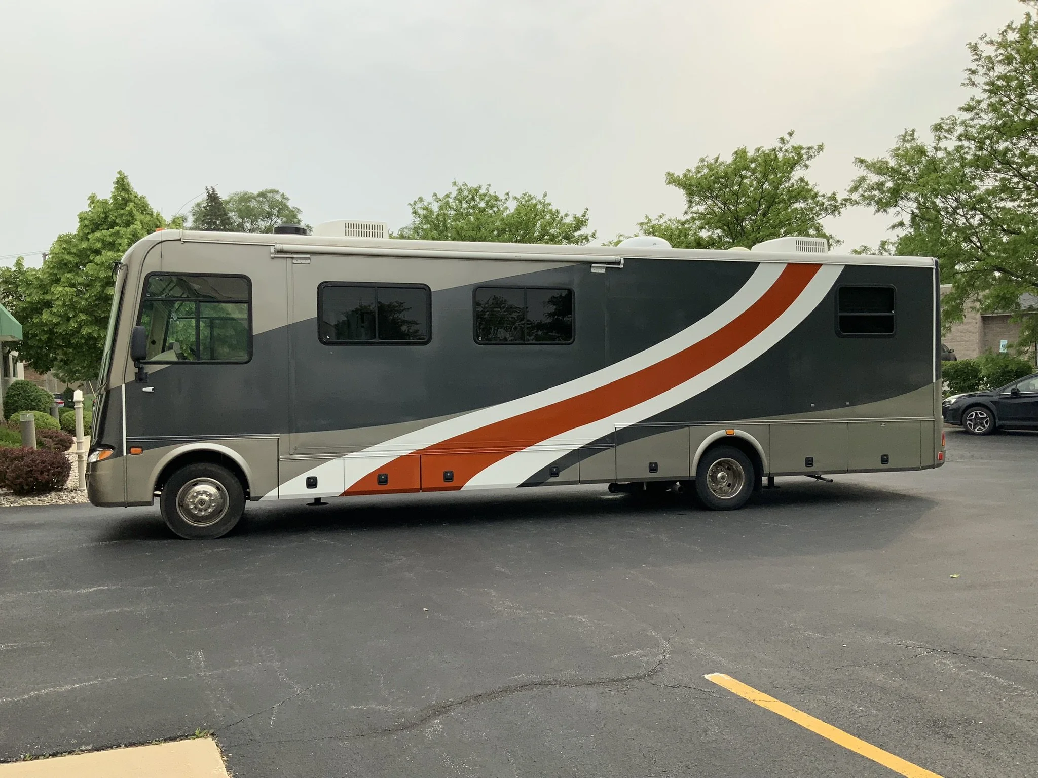 A recreational vehicle (RV) parked on a parking lot, with trees and a cloudy sky in the background.