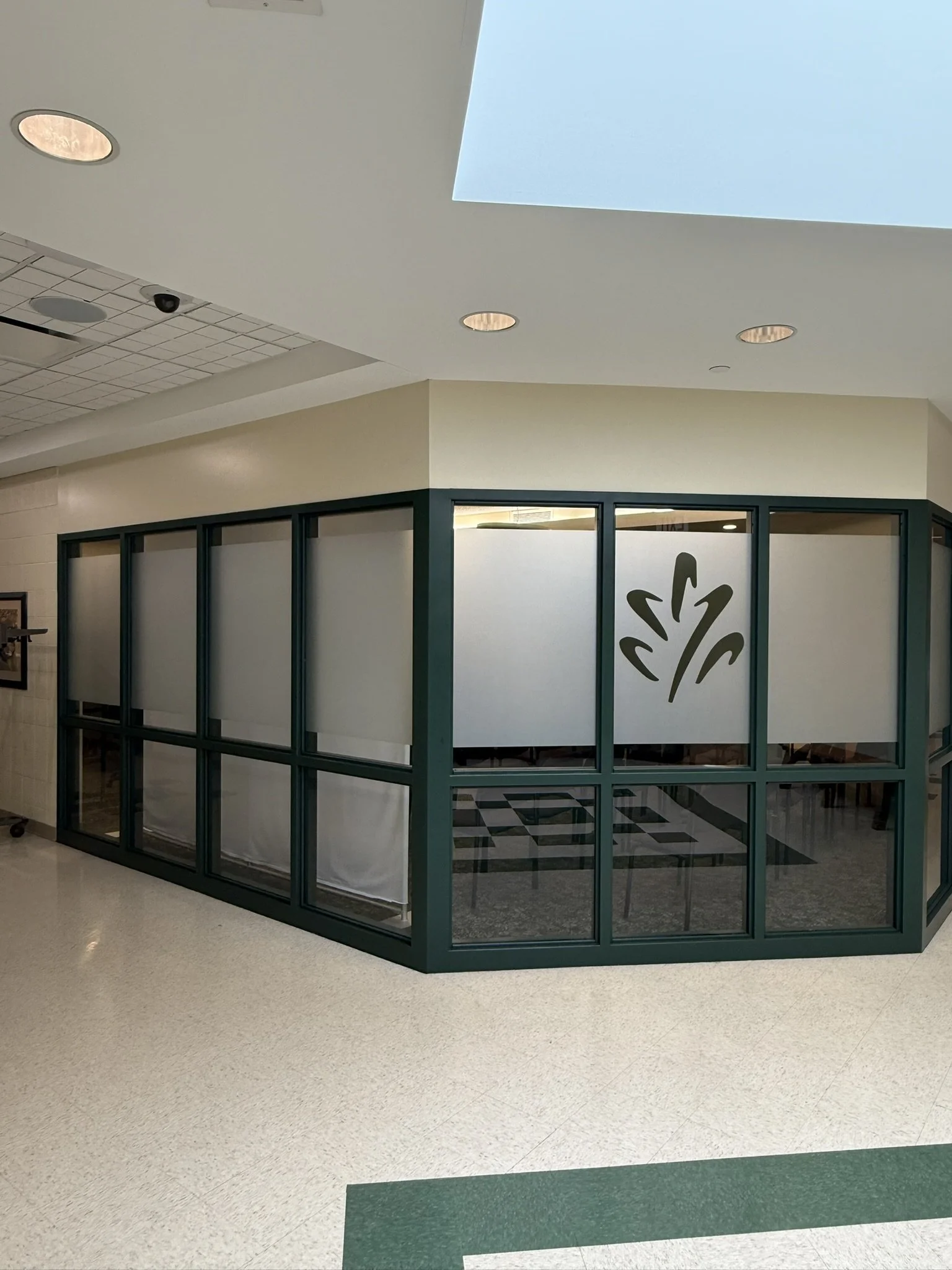 Interior view of a closed information booth with glass panels and a logo, situated in a hallway with beige and green flooring.