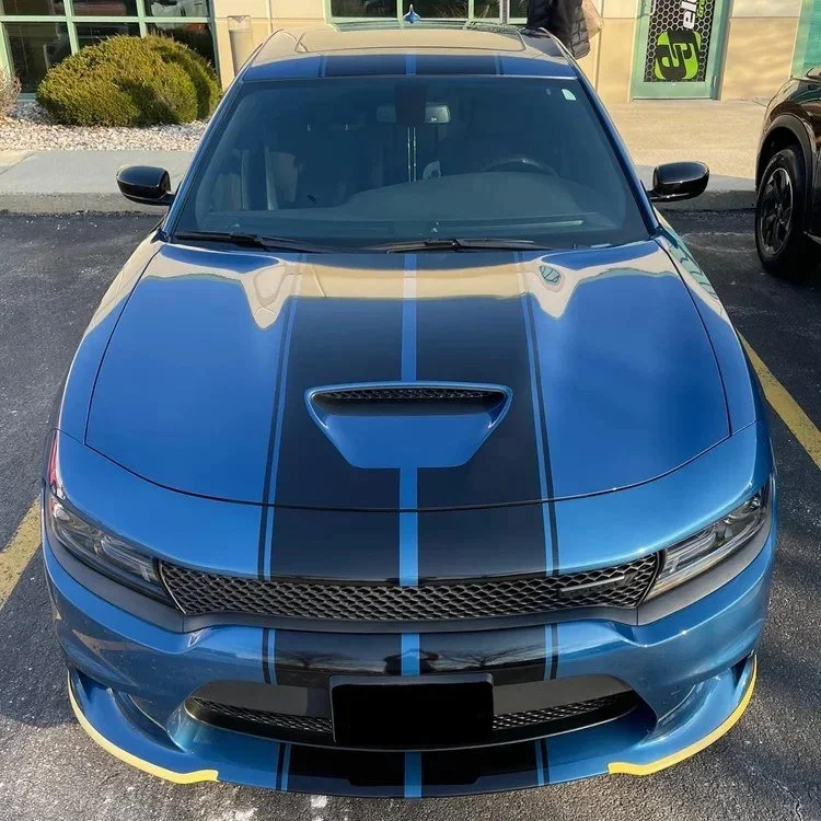 Front view of a blue sports car with black racing stripes and a hood vent, parked in a parking lot.