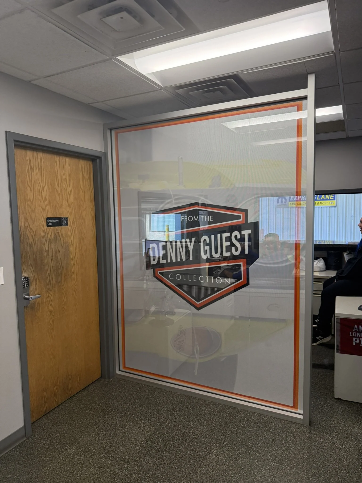 Office interior with a door marked 'Employees Only' and a large glass panel with a sign that says 'From the Penny Guest Collection' in a retail or office environment.