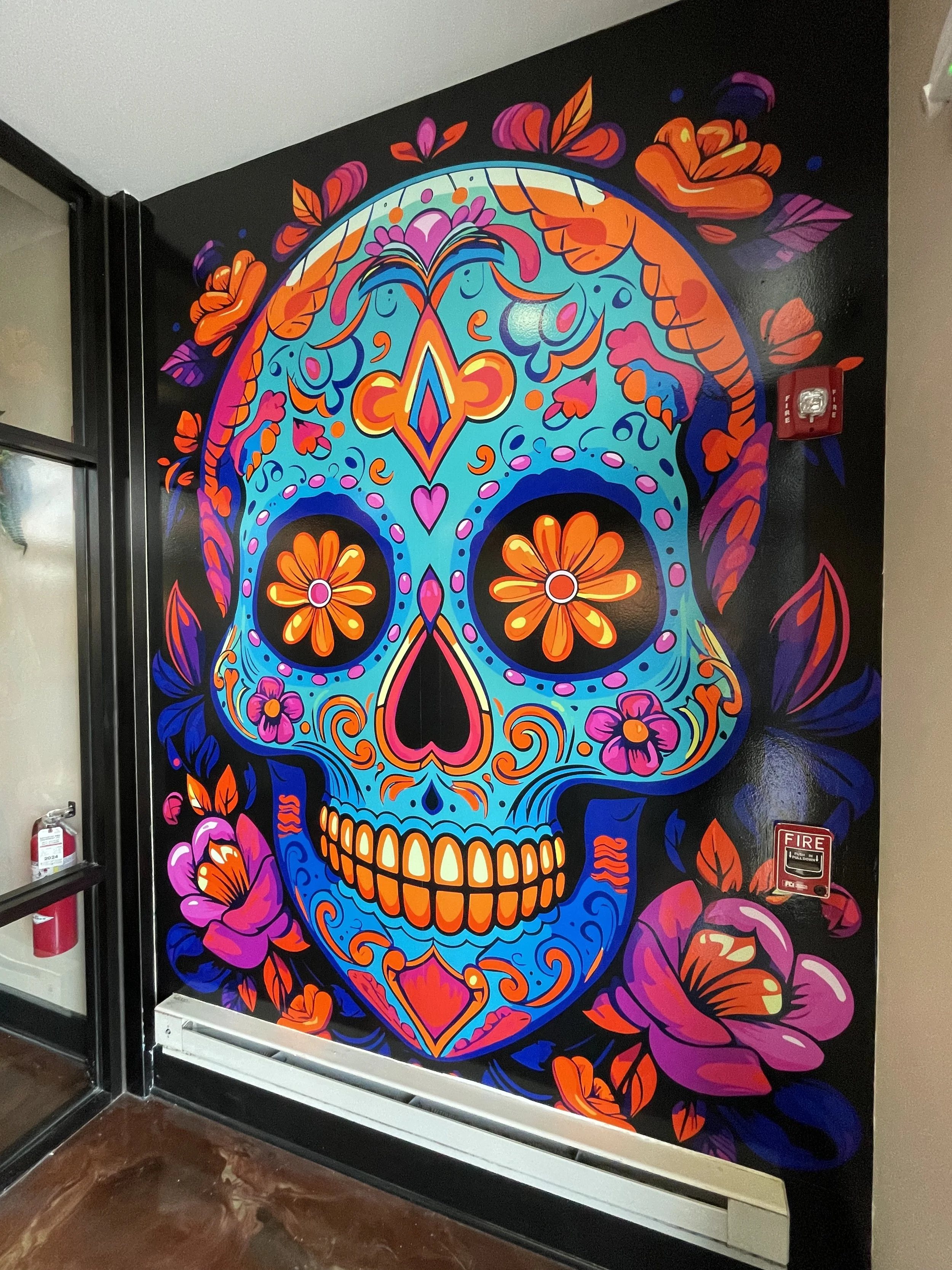 Colorful mural of a decorated sugar skull with floral patterns on a black background in a hallway.