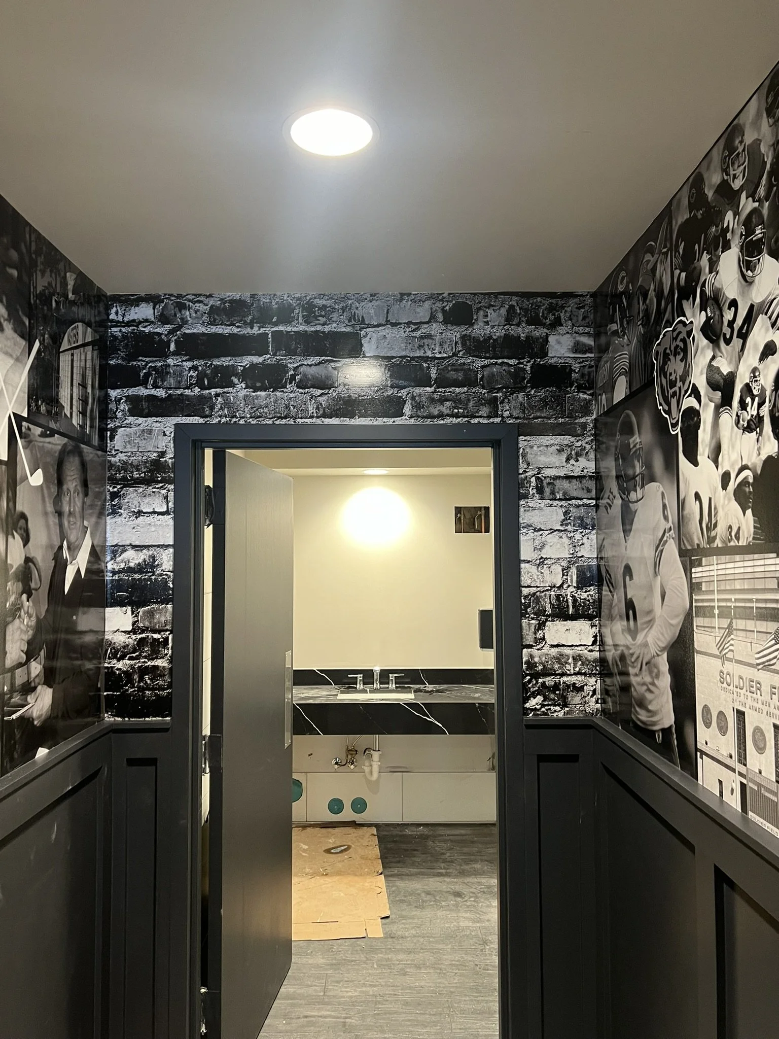 Interio of a room with black and white sports-themed wall art, a small bathroom with marble countertop visible through an open doorway, and a ceiling light.