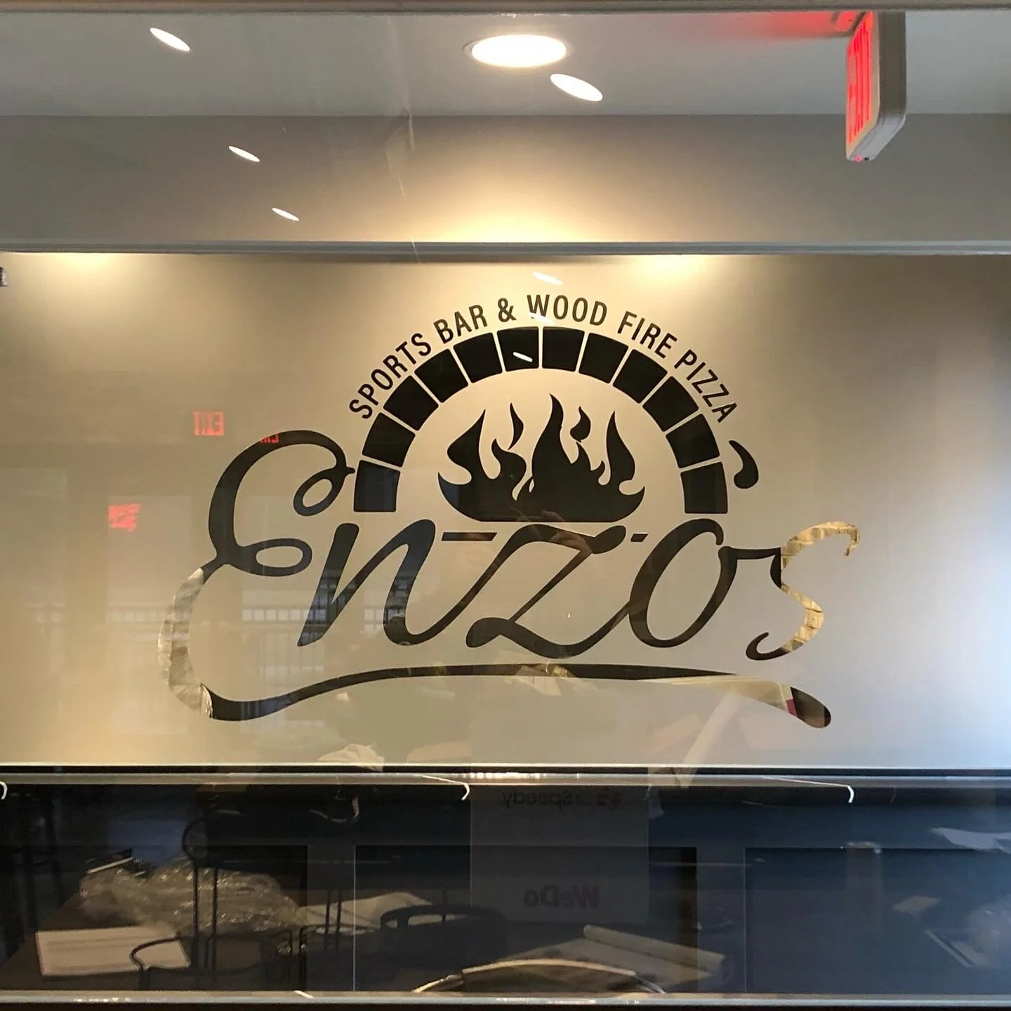 Glass window with logo for 'Snizos' restaurant featuring a stylized flame, pizza oven arch, and the text 'Sports Bar & Wood Fire Pizza'.