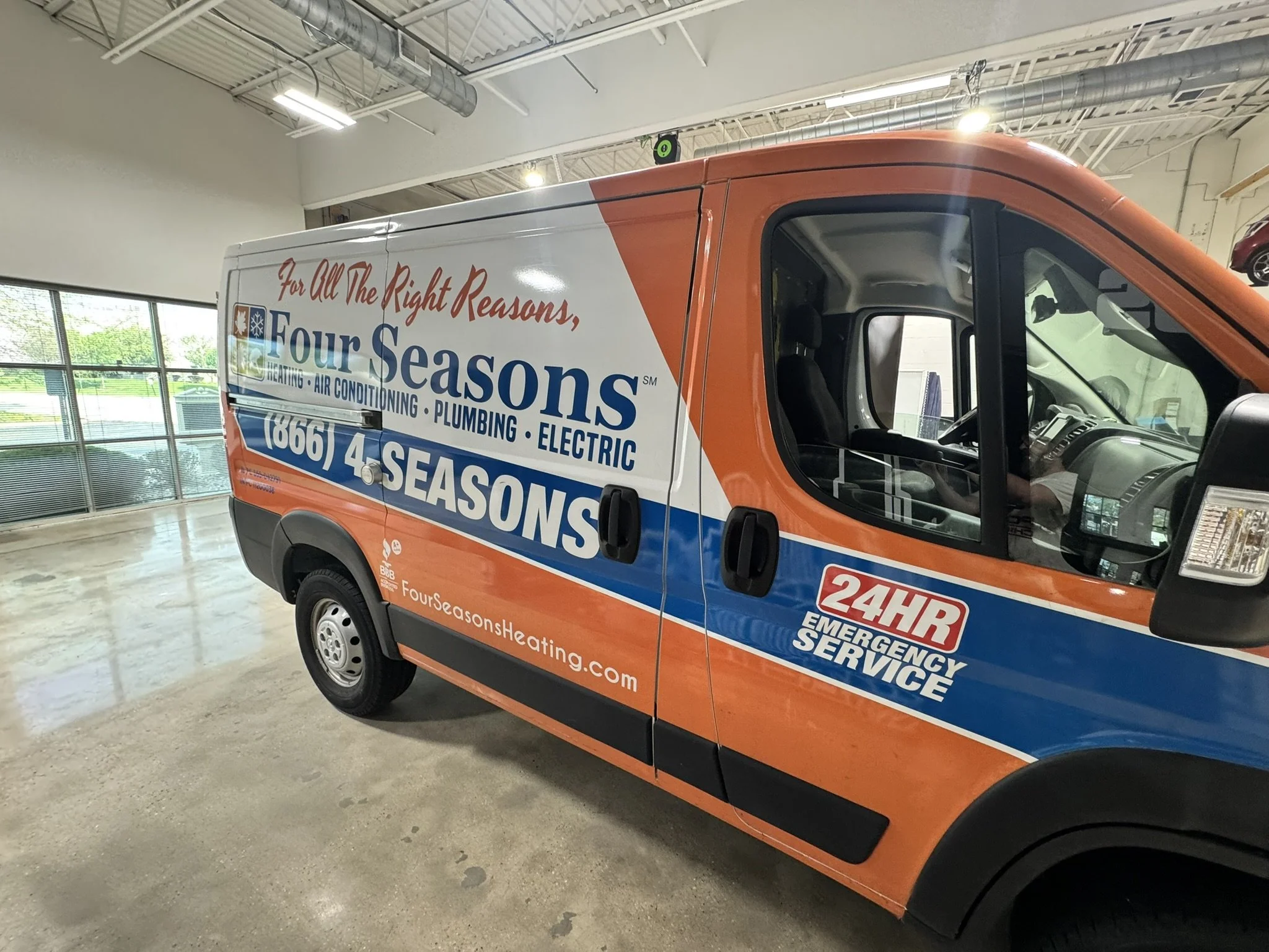 A service van for Four Seasons Heating, Cooling, Plumbing, and Electric inside a building with a concrete floor, large windows, and a high ceiling.