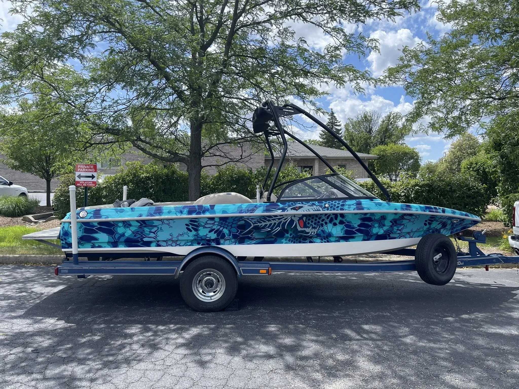 Colorful speedboat with a blue, black, and orange design on a trailer parked on a street, with trees and houses in the background.