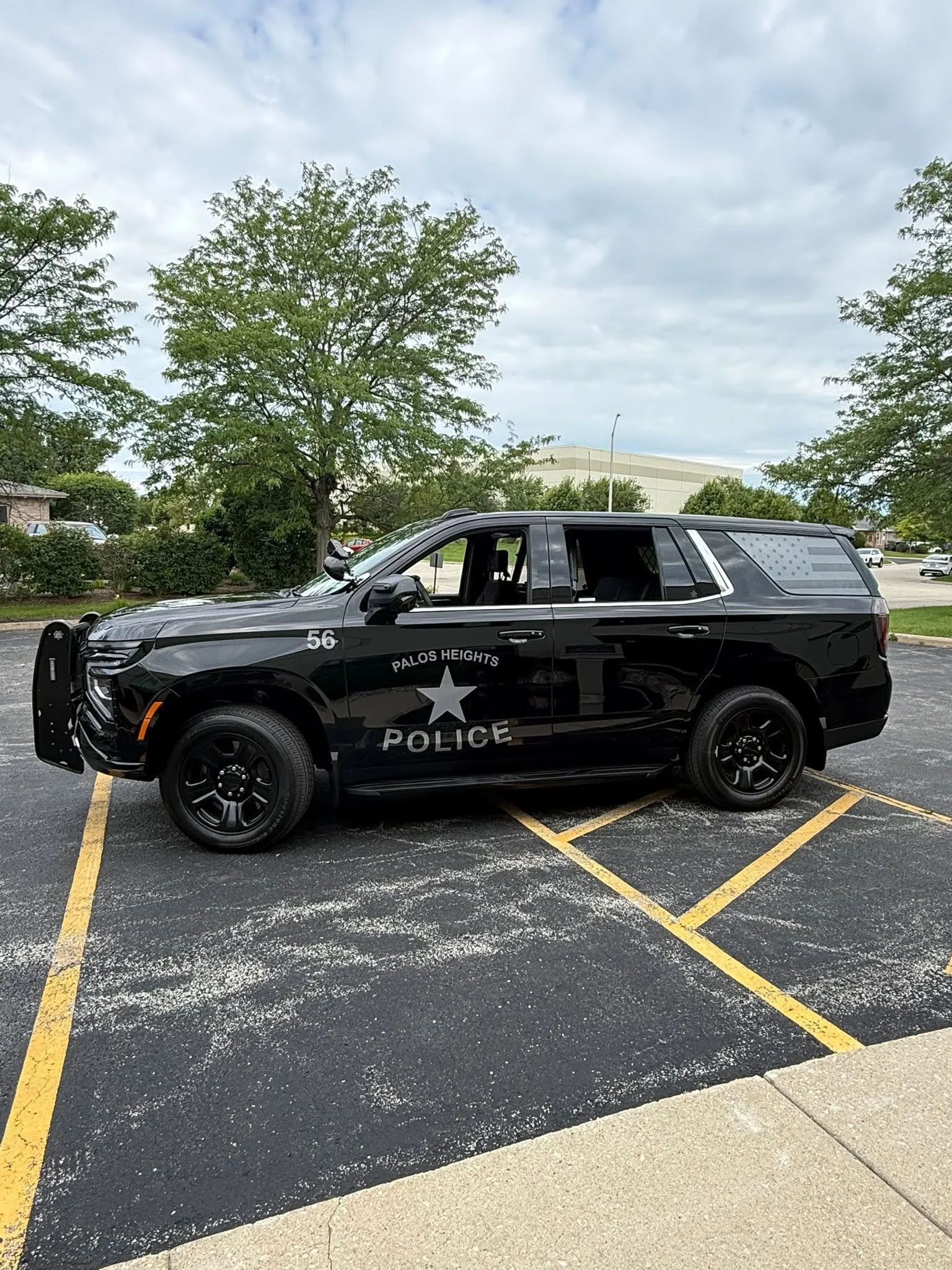 Black Palos Heights Police SUV parked in a parking lot with trees and a cloudy sky in the background.