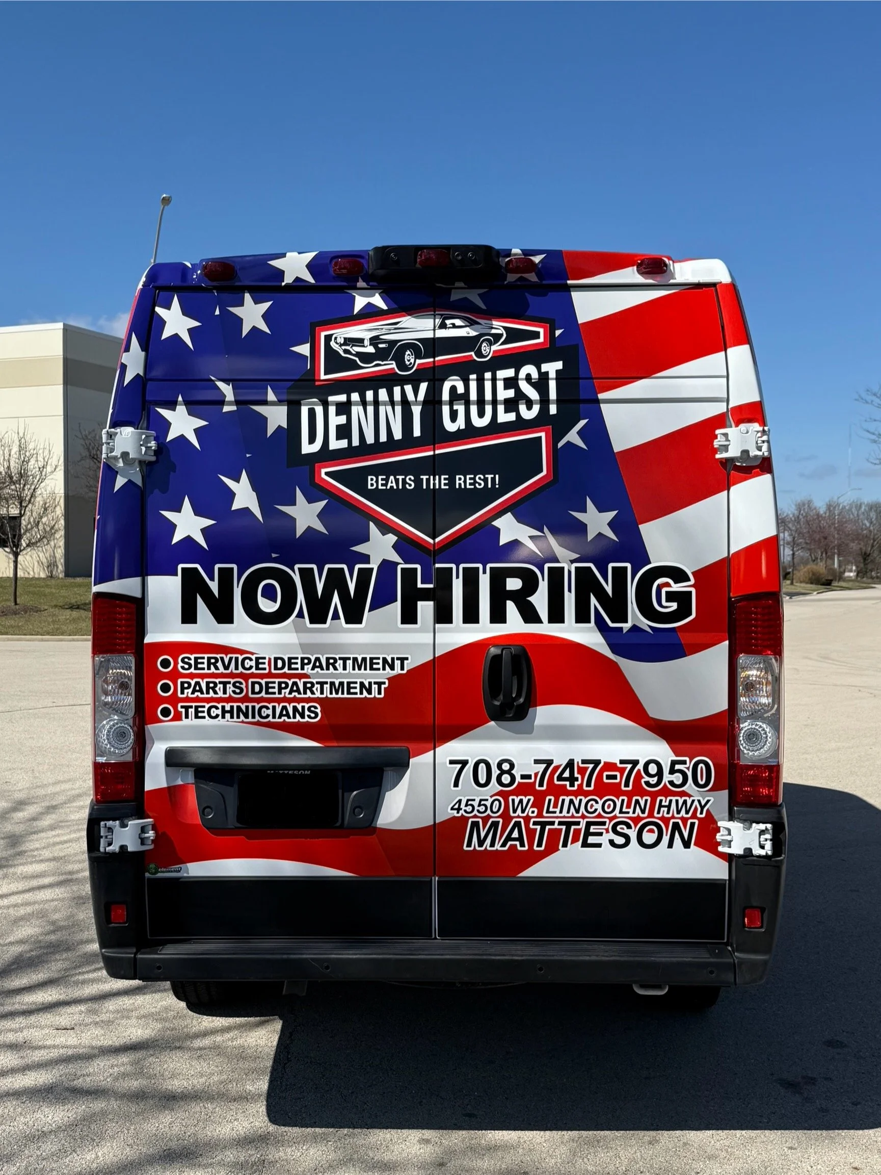 Back of a red, white, and blue vehicle with American flag design, advertising a job opening at Denny Guest with contact information and a car graphic.