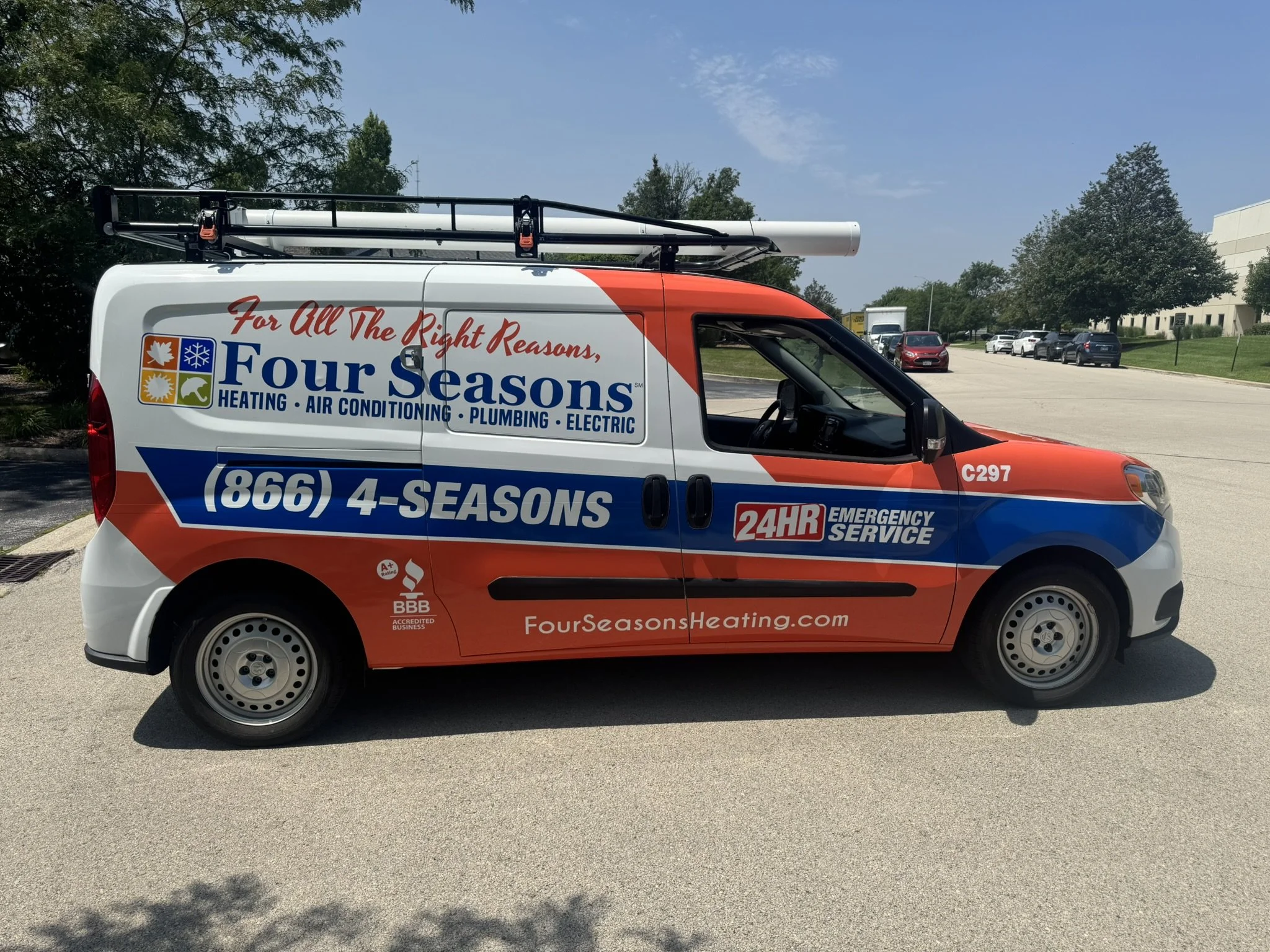 A service van for Four Seasons Heating, Air Conditioning, Plumbing, and Electric, parked in a parking lot with trees and other vehicles in the background. The van has the company logo, phone number, and website on the side.