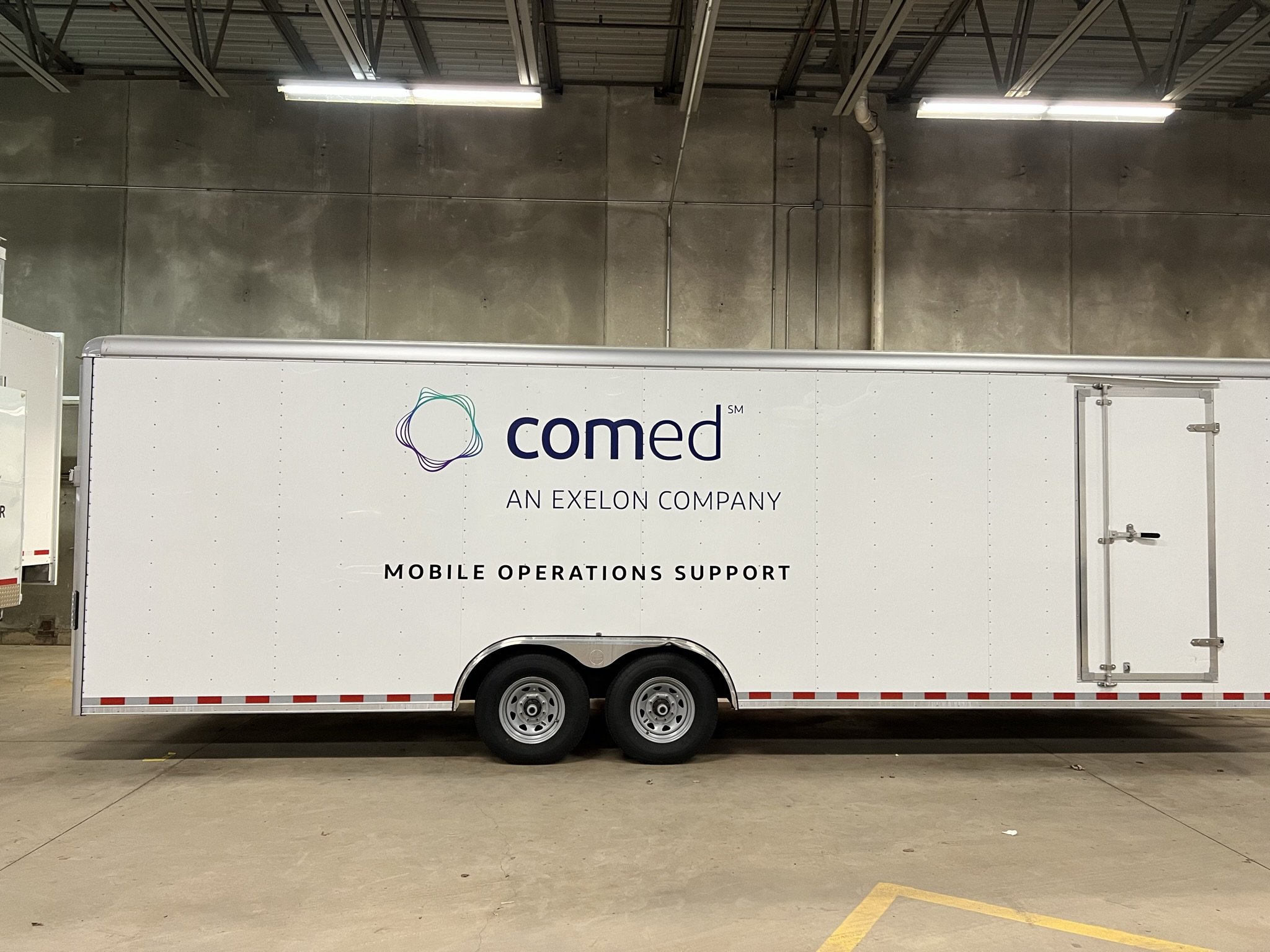 A white truck parked inside a large industrial or warehouse space with a concrete wall and ceiling. The truck displays the logo and text 'comd Alternative' and 'An Exelon Company' along with 'Mobile Operations Support'.