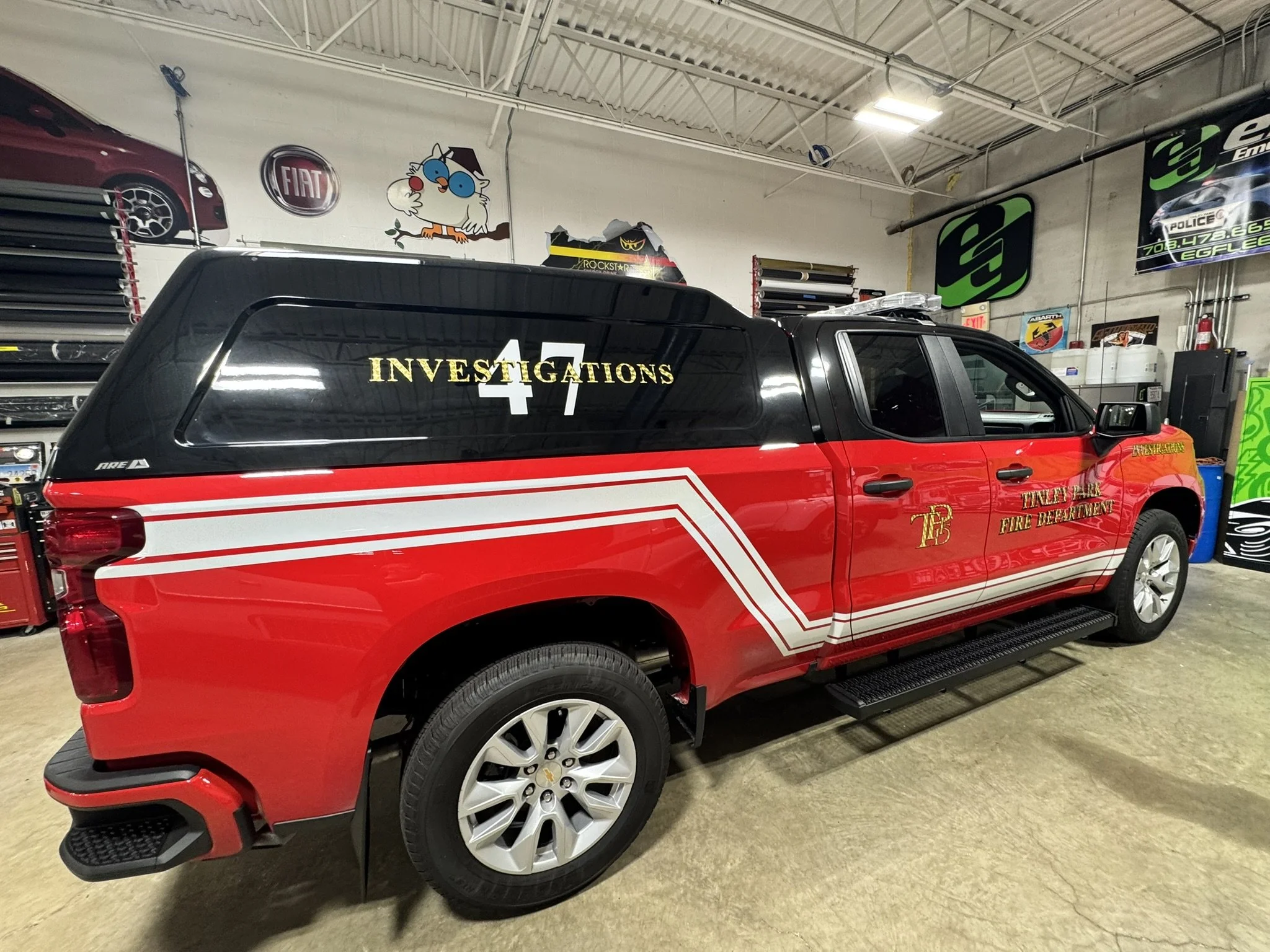 Red and black emergency vehicle with 'Investigations 4T' written on the side, parked inside a garage with automotive and promotional signs on the wall.