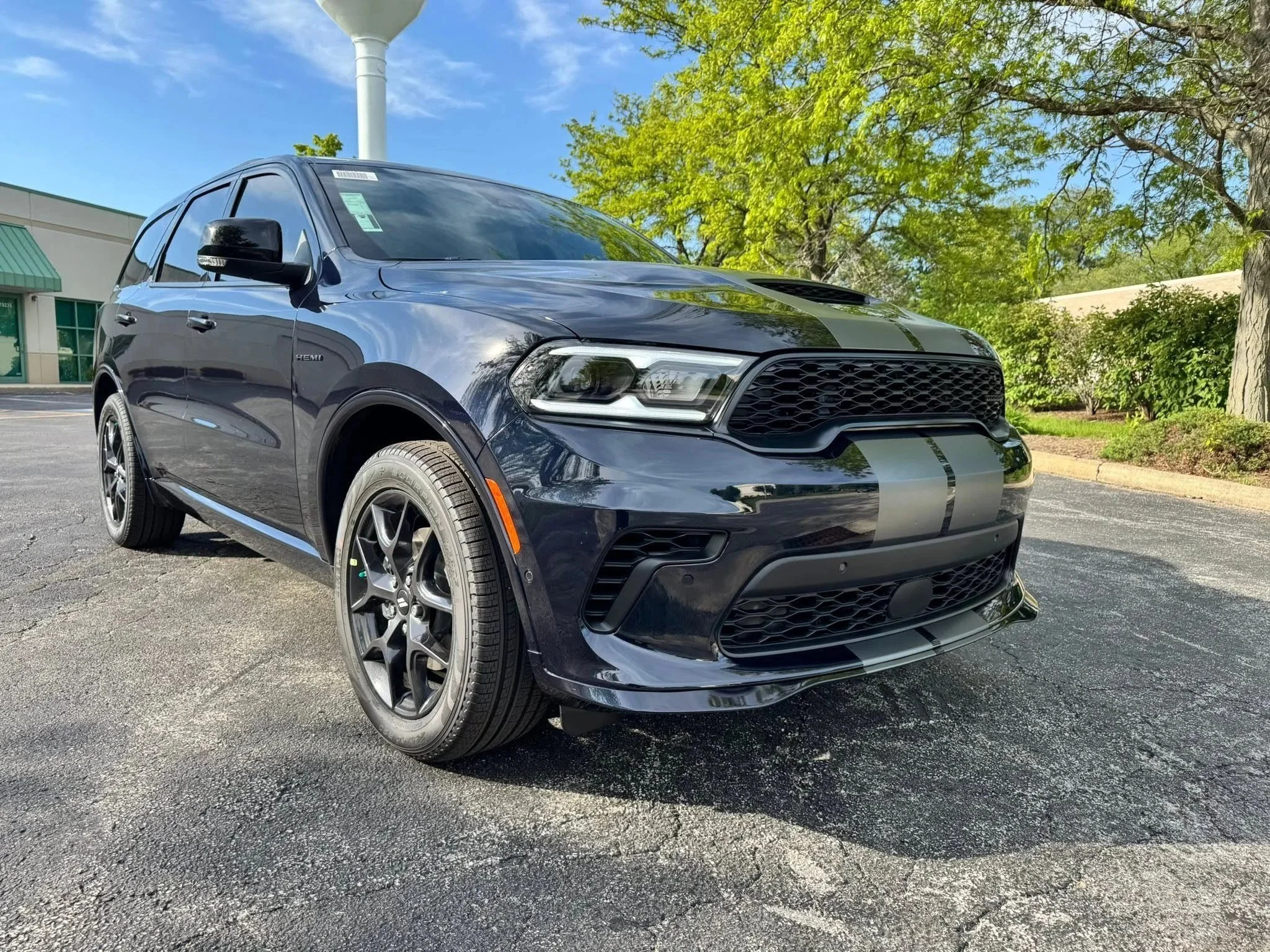 A black Dodge Durango parked outdoors on a paved lot with green trees and a building in the background during daytime.