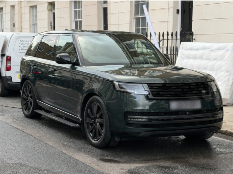 Black Range Rover SUV parked on street near white building with black gate.