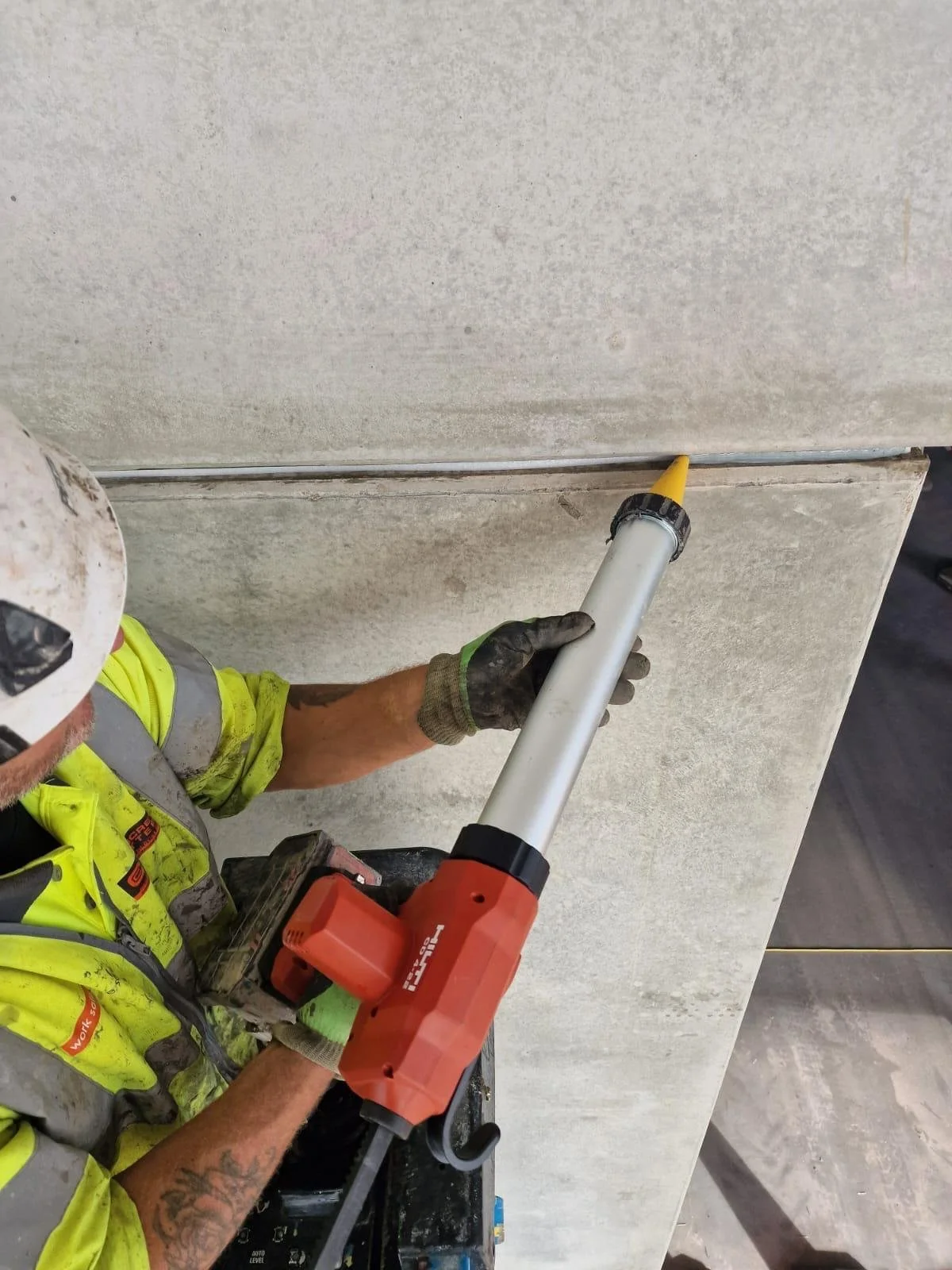 Construction worker using a red Hilti power tool to work on a concrete surface.