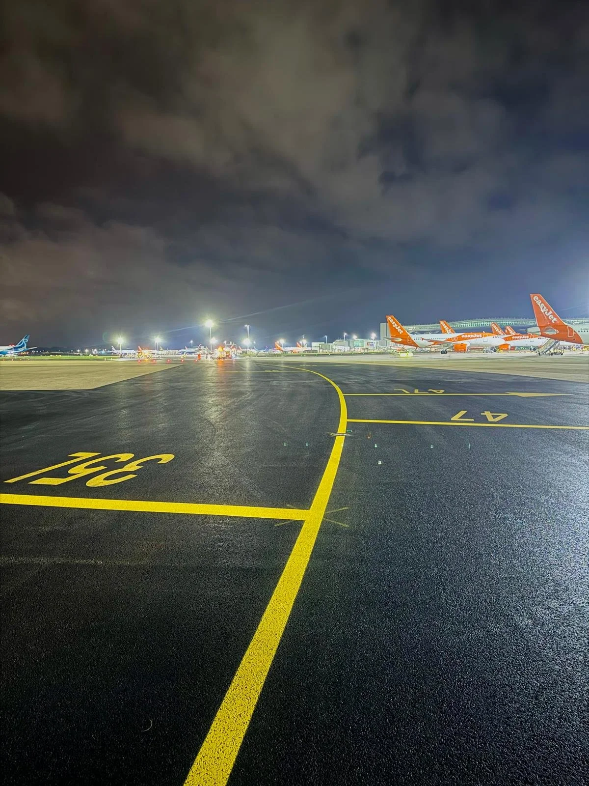 Nighttime airport tarmac with multiple parked orange AirAsia airplanes under illuminated terminal lights.