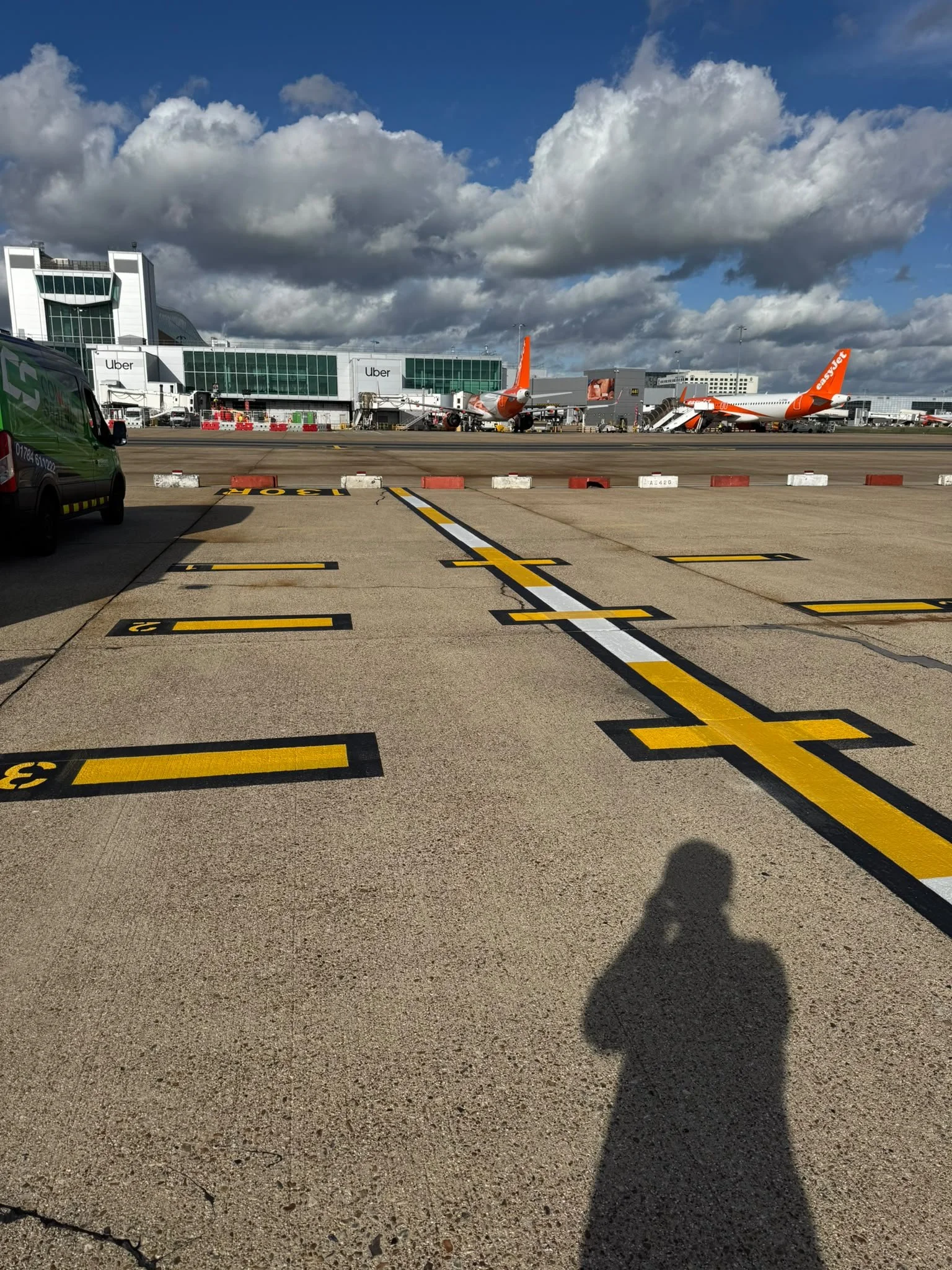 EasyJet aircraft parked at an airport terminal beneath dramatic clouds, with runway markings and an airport service van in the foreground