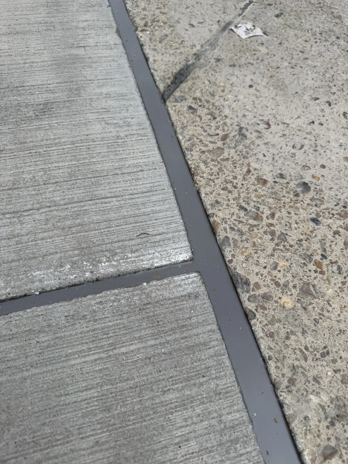 Close-up of gray concrete pavement with dark expansion joint sealant between slabs and rough aggregate concrete.
