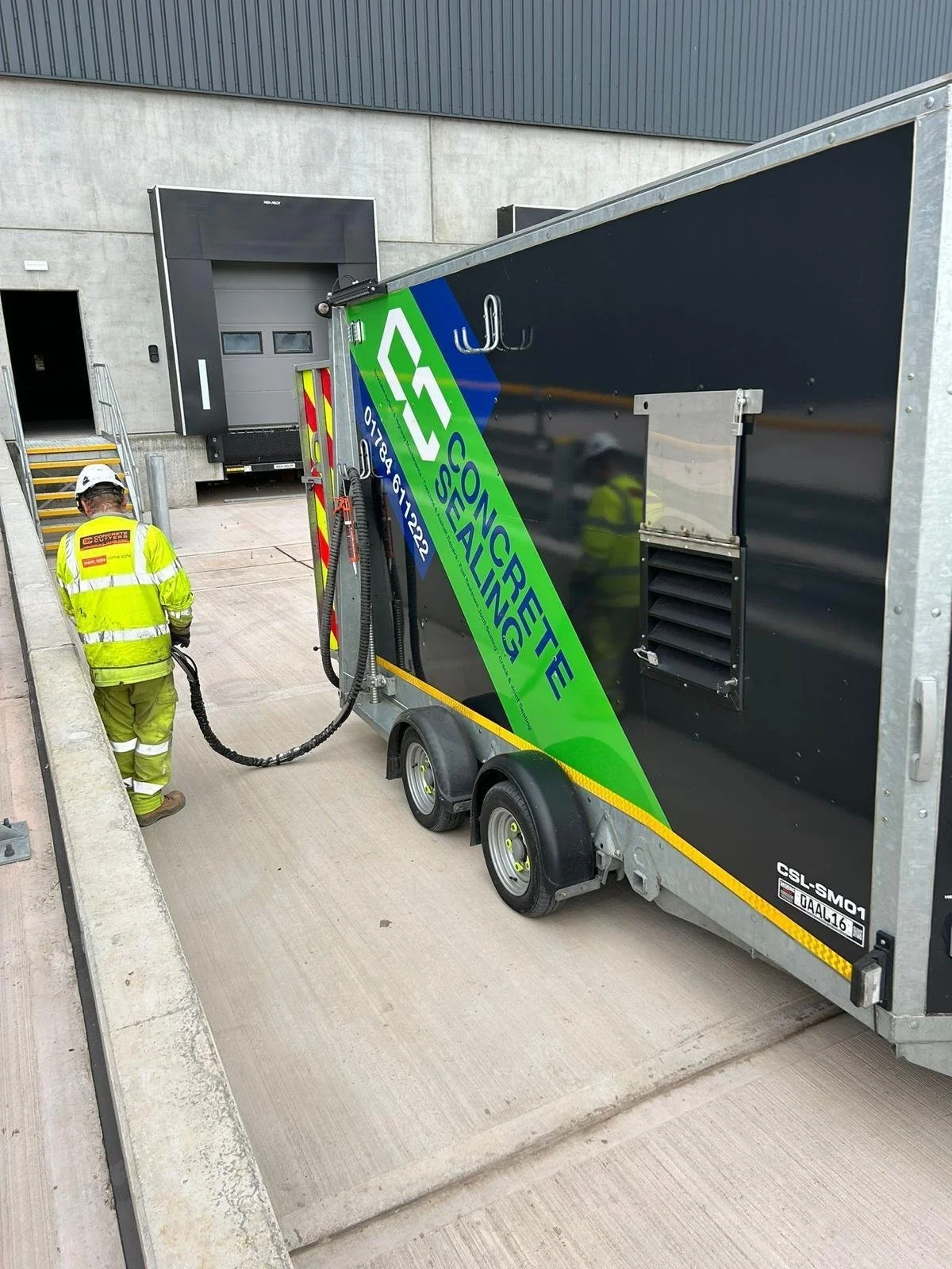 Worker in high-visibility clothing beside a branded mobile welfare trailer at an industrial loading dock