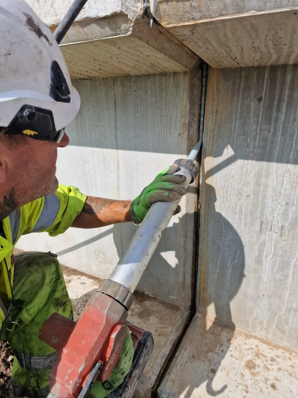 Construction worker in safety gear using a power tool on a concrete structure