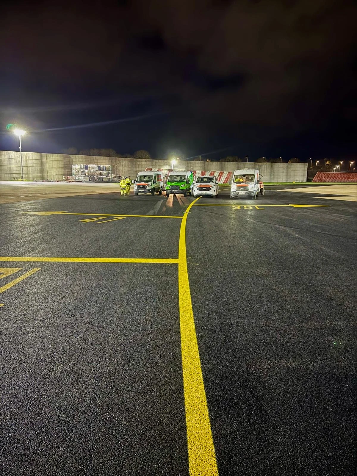 Four service vans and airport ground crew on a brightly lit airport tarmac at night