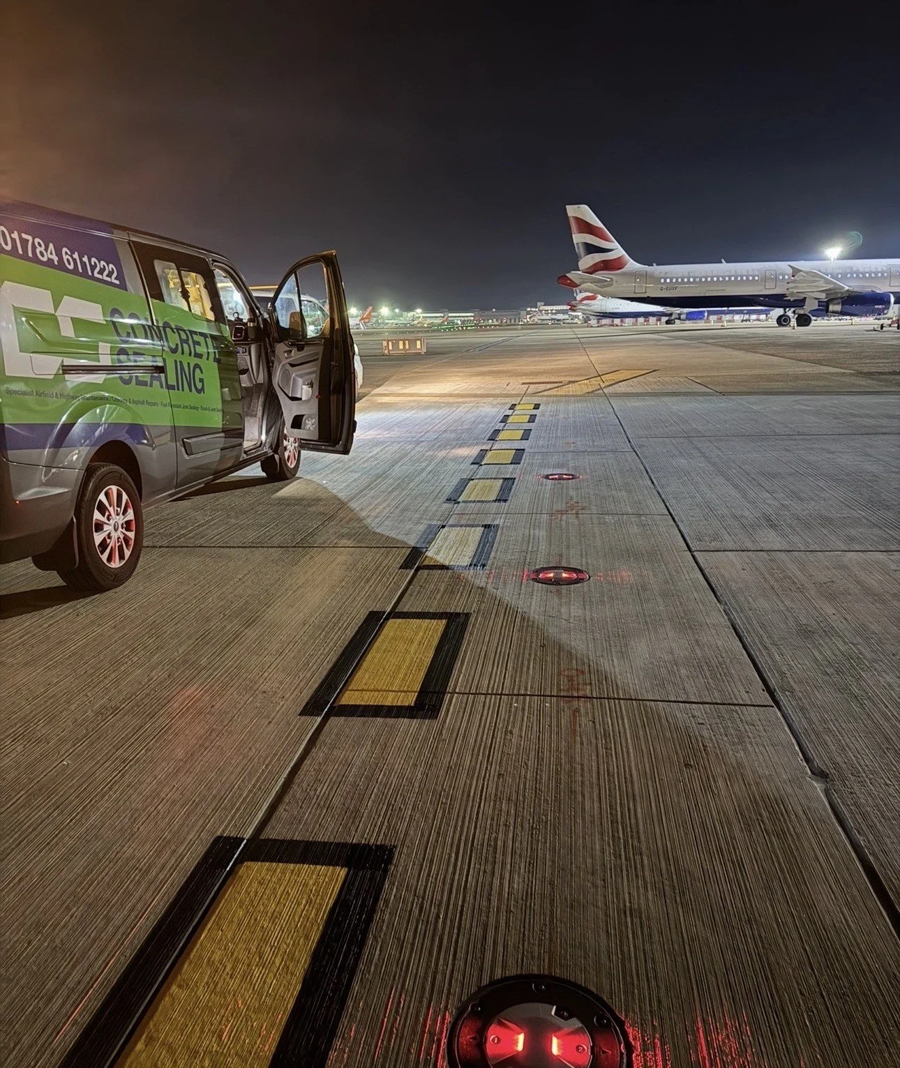Airport runway at night with a branded airport ground-service van and a British Airways passenger plane.