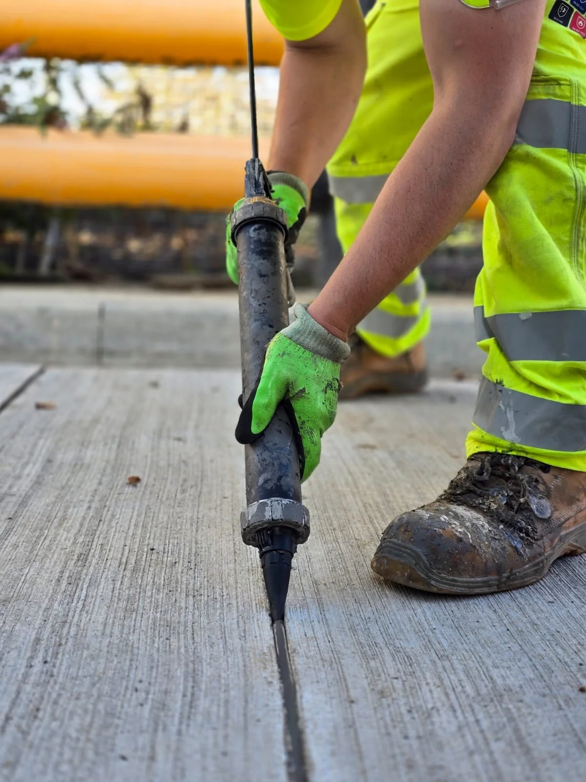 Construction worker in high-visibility clothing uses a concrete saw to cut a pavement joint.