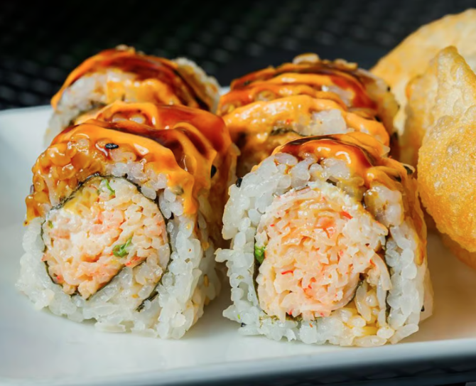 Close-up of four sushi rolls topped with spicy sauce, served with tempura chips on a white plate.