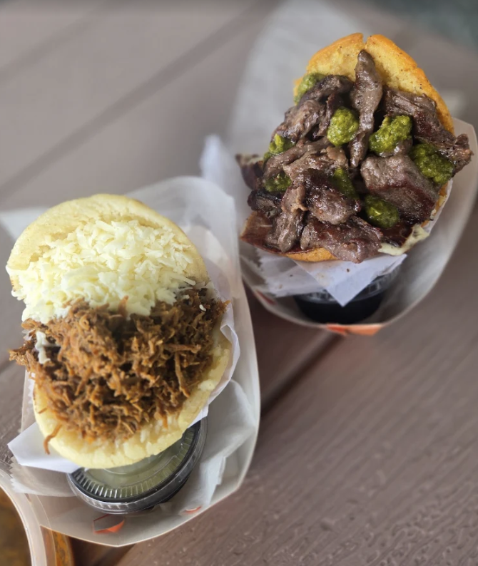 Two sandwiches, one with shredded pork and mashed potatoes, and the other with beef stew and green peppers in a bun, placed on a wooden surface.
