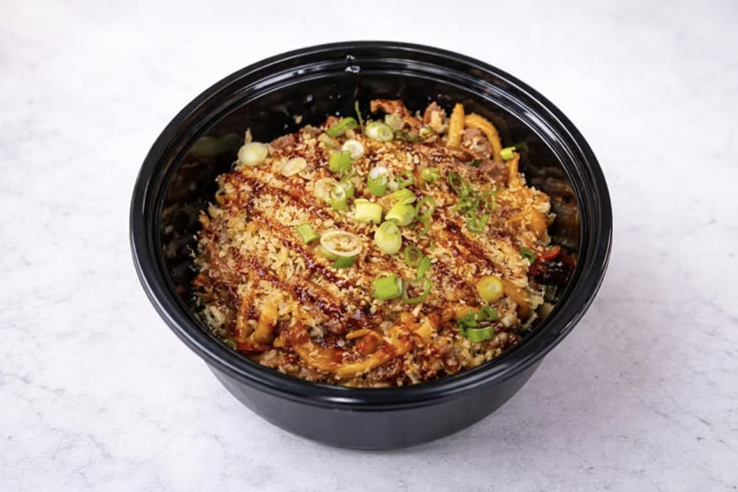 Takeout bowl of Asian-style ground meat and vegetable stir-fry topped with chopped green onions.