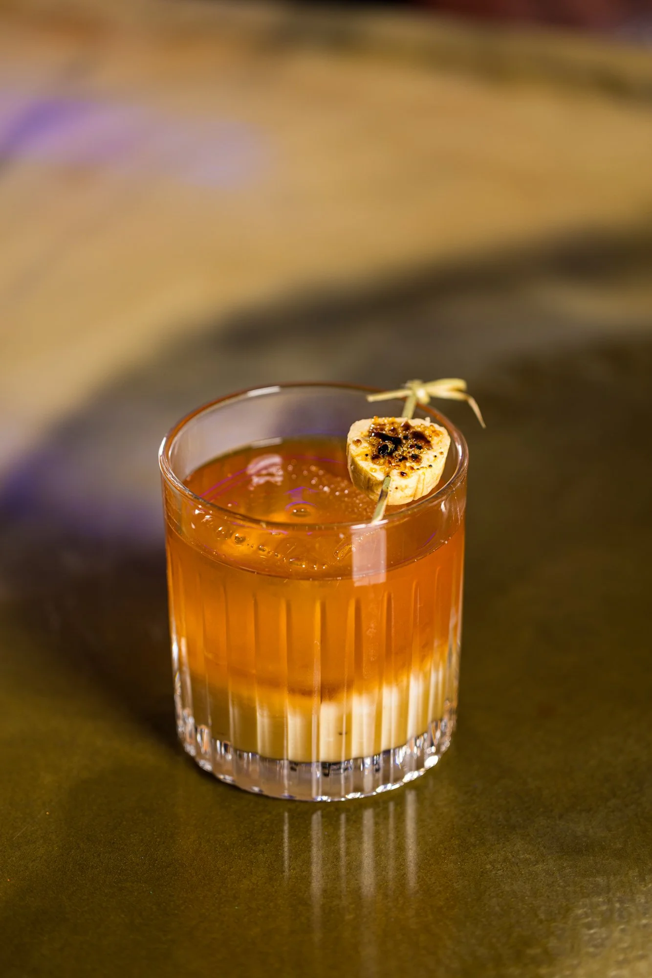 A glass of orange-colored cocktail garnished with a toasted marshmallow on a skewer