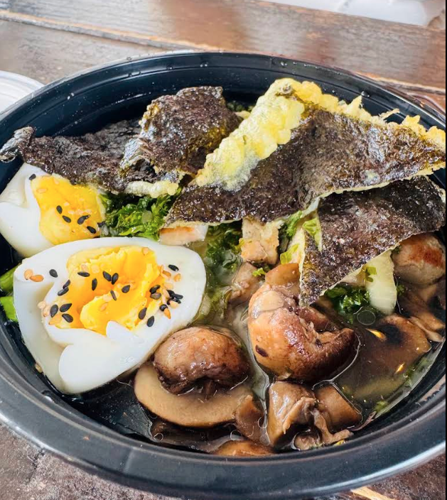 A bowl of ramen with soft-boiled eggs, seaweed, mushrooms, and green vegetables.