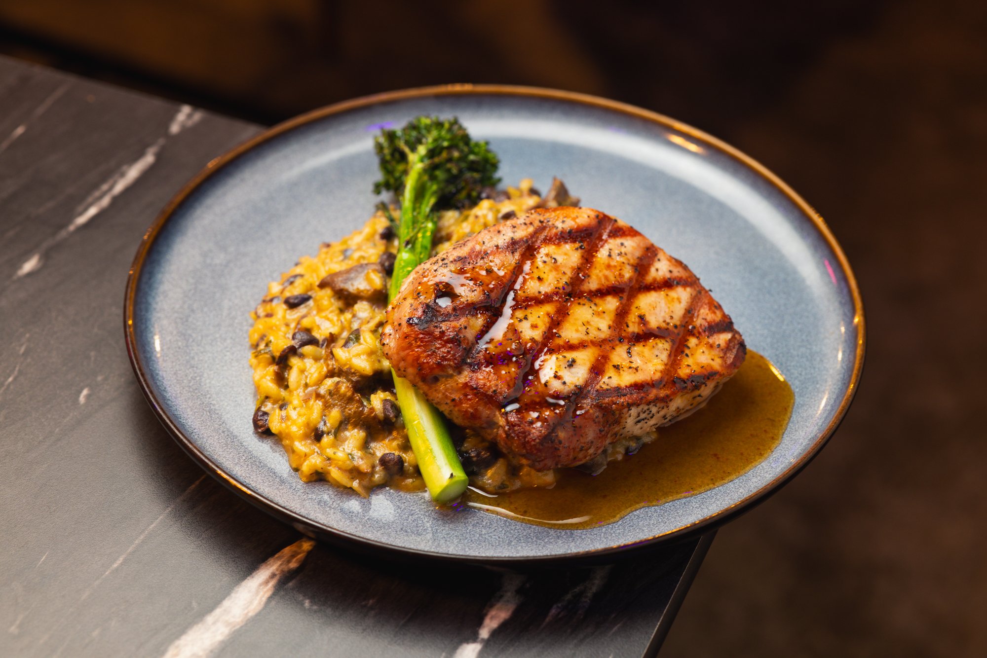 A grilled chicken breast topped with sauce, served with rice and vegetables including broccoli and mushrooms on a ceramic plate.