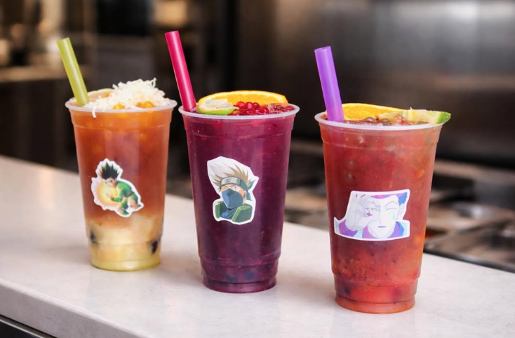 Three colorful fruit smoothies with characters' stickers on clear cups, each with a different colored straw, placed on a white countertop.