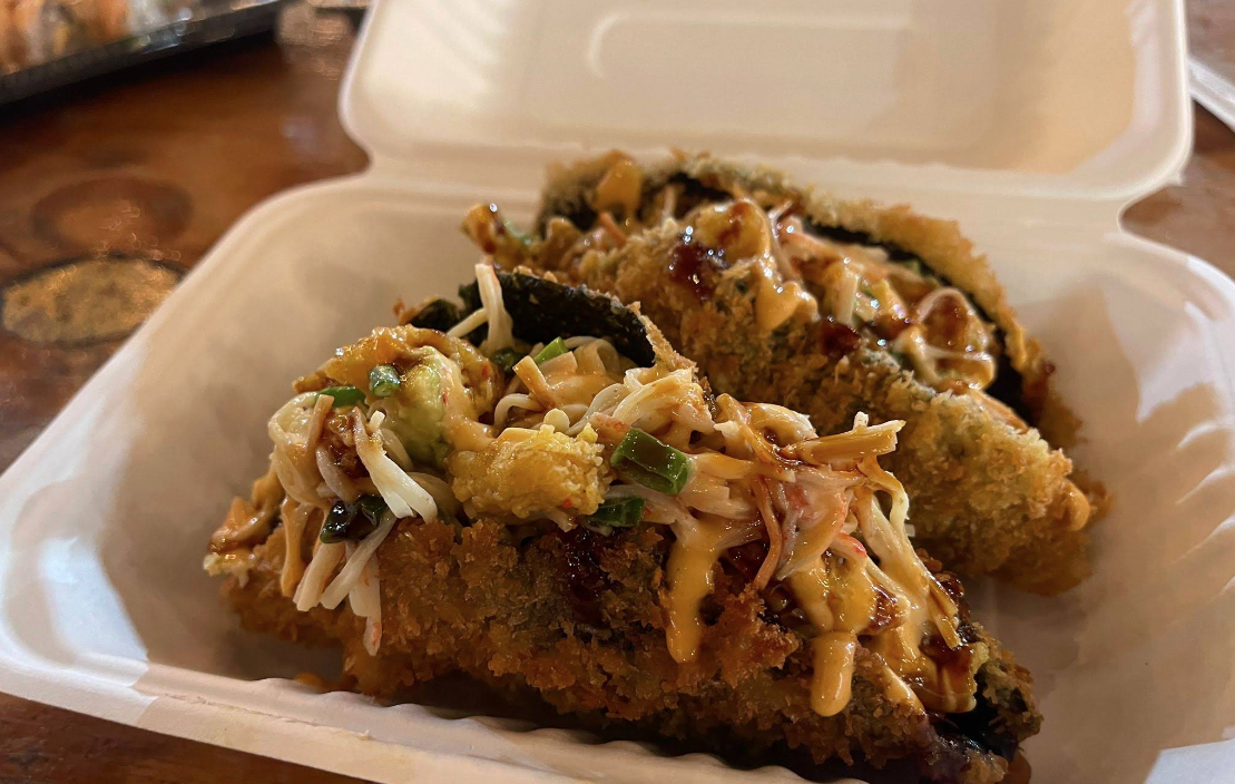 Two pieces of deep-fried fish served with coleslaw, inside a white takeout container on a wooden table.