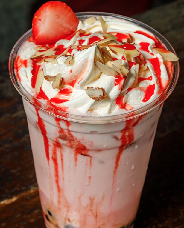 A beverage with whipped cream, strawberry topping, almond slices, and red syrup in a glass.