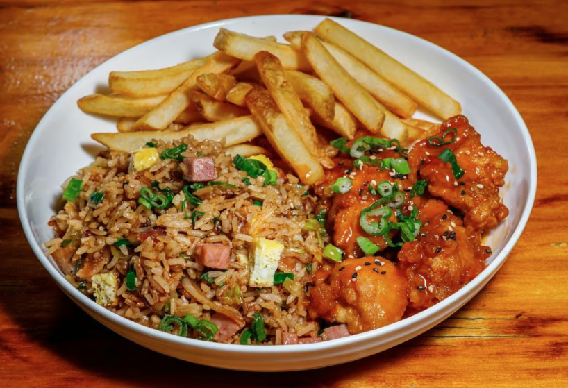 Bowl of Chinese-style fried rice with chopped ham and green onions, crispy French fries, and orange chicken garnished with green onions and sesame seeds.