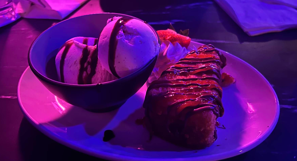 Ice cream scoop and a dessert on a white plate under purple lighting