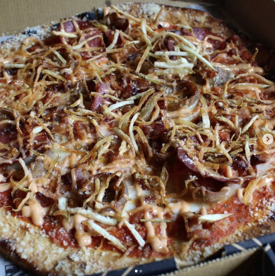 Close-up of a freshly baked pizza with crispy crust, topped with shredded beef, fried onions, melted cheese, and drizzled with a creamy sauce.