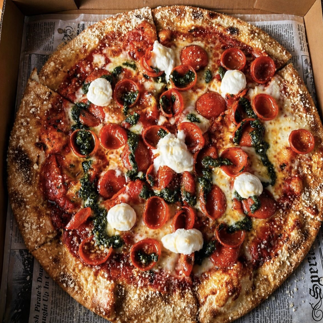A pepperoni, mozzarella, and basil pizza in a box with newspaper lining.