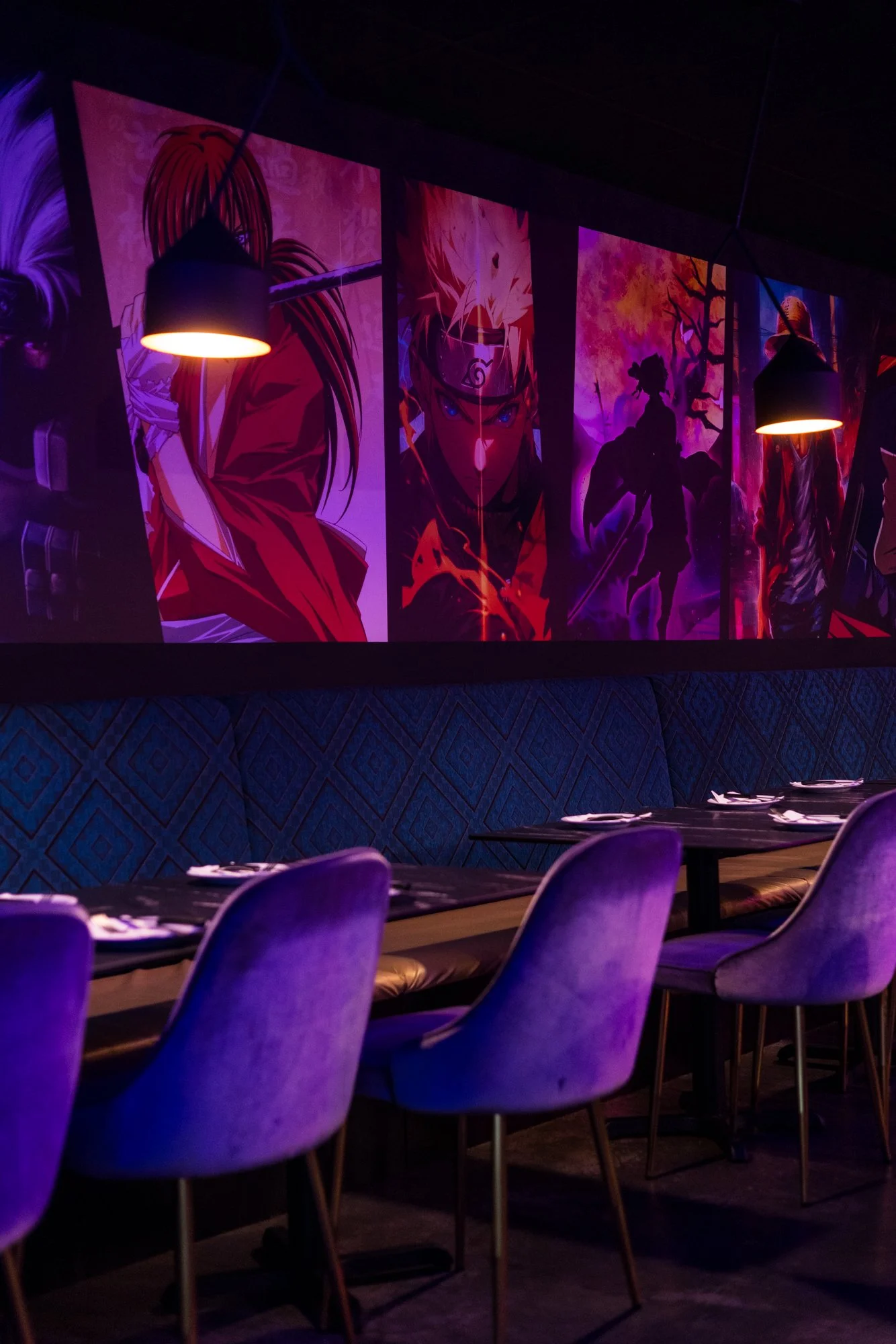 A restaurant interior with colorful wall art featuring anime characters illuminated by purple and orange lighting. There are purple chairs and tables set for dining.
