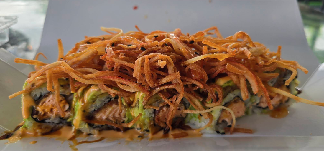 Close-up of a sushi roll topped with crispy fried onions and drizzled with sauce.