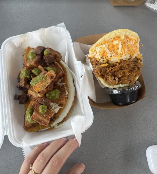 Two pulled pork sandwiches with cheese on yellow buns, served with fried okra in a foam container and a pork tamale in a paper tray.