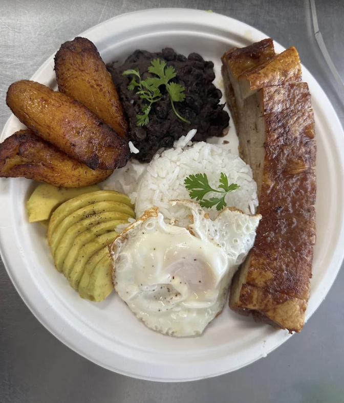 A plate of Colombian breakfast with fried plantains, black beans, white rice with cilantro, avocado slices, a fried egg, and fried fish.