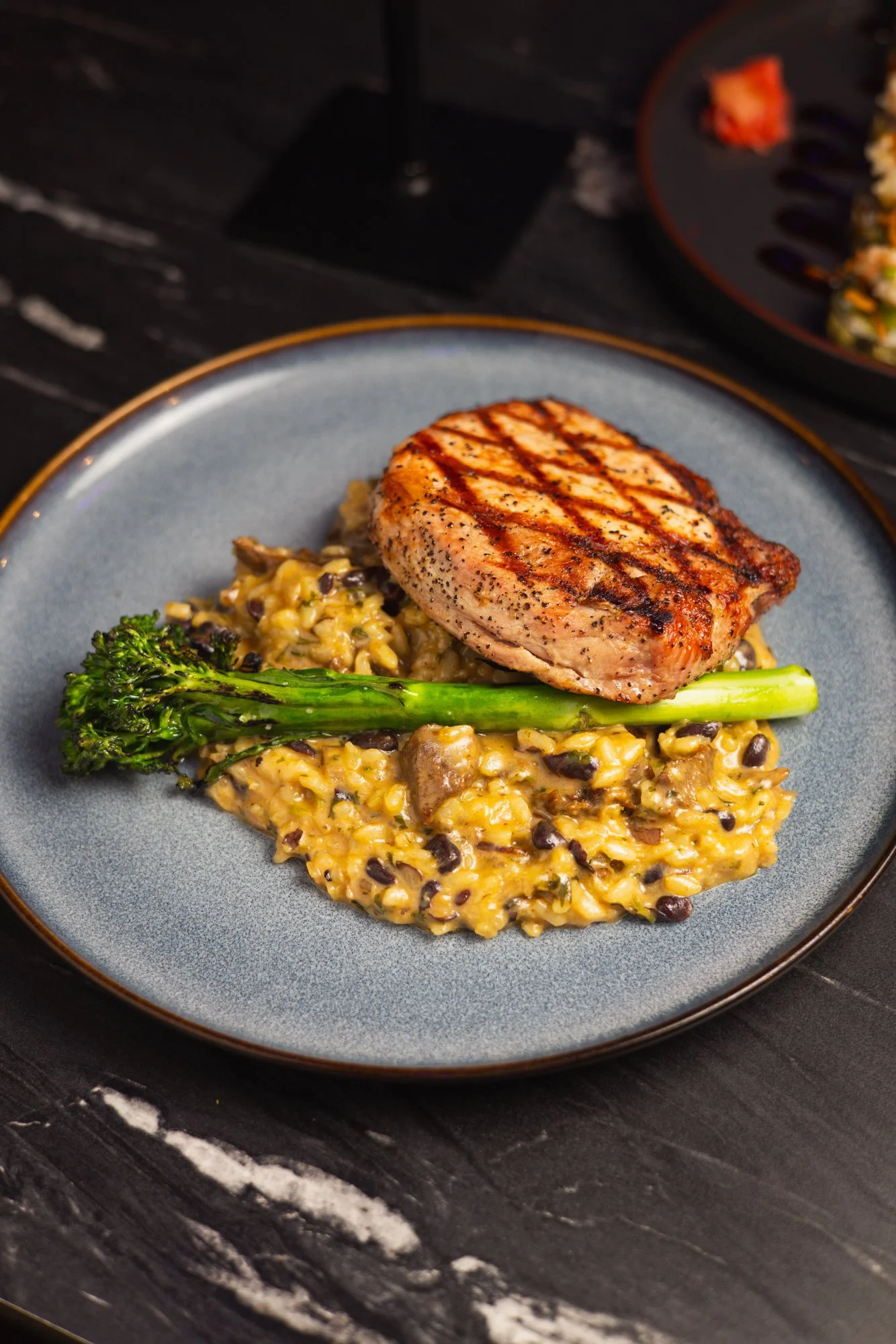 Grilled chicken breast with black pepper on top, served with seasoned rice and a broccoli stalk on a gray plate.