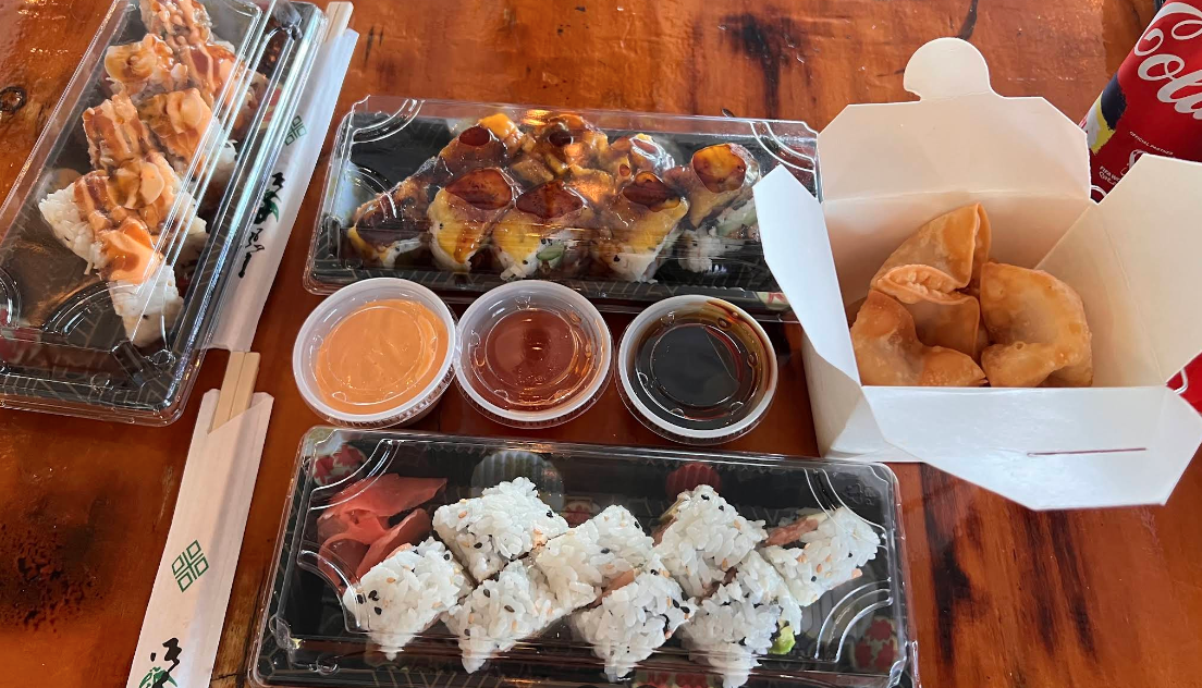 Assorted Japanese sushi rolls, fried dumplings, and sushi with eel and rice, accompanied by soy sauce, spicy mayo, and eel sauce, arranged on a wooden table.