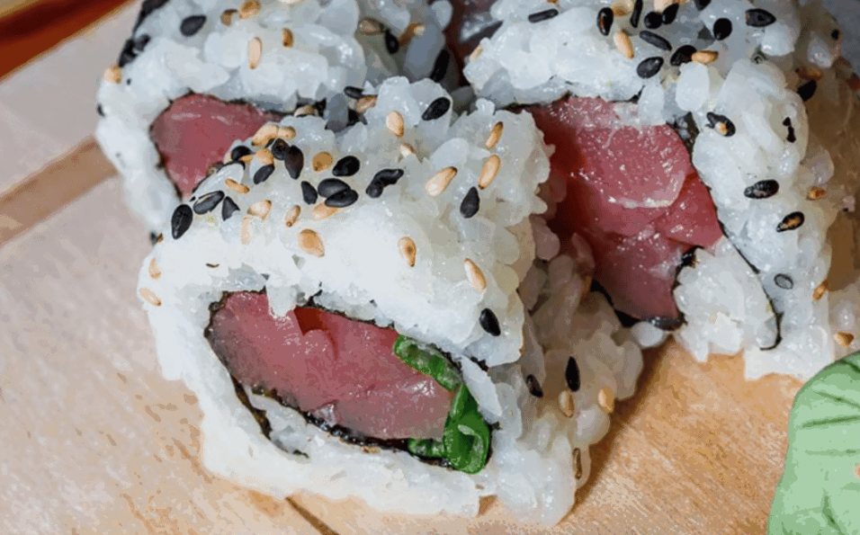 Close-up of sushi rolls filled with raw tuna, rice, and green vegetable, topped with sesame seeds.