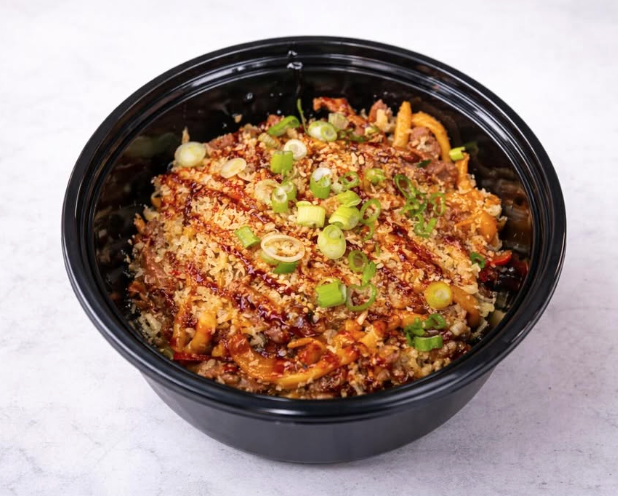 A black bowl of Asian-inspired noodle dish topped with chopped green onions and breadcrumbs.