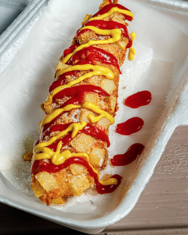 Fried sushi roll topped with ketchup and mustard, served in a white foam container on a wooden surface.