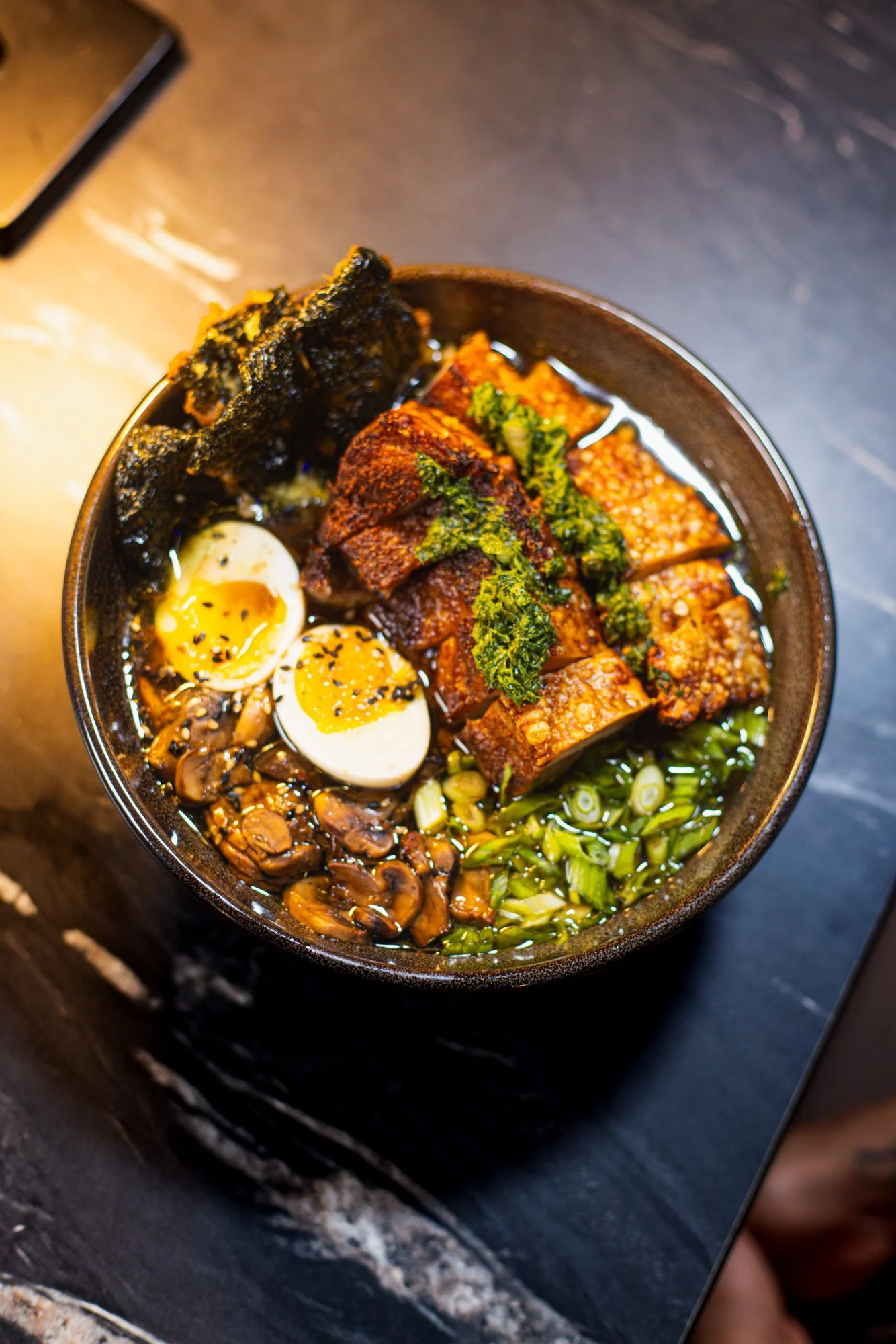 A bowl of ramen with soft-boiled eggs, sliced pork, chopped green onions, mushrooms, seaweed, and various toppings.